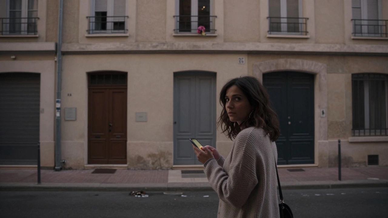 A woman on a Marseille street at dusk, holding a phone, standing before an unmarked apartment building.